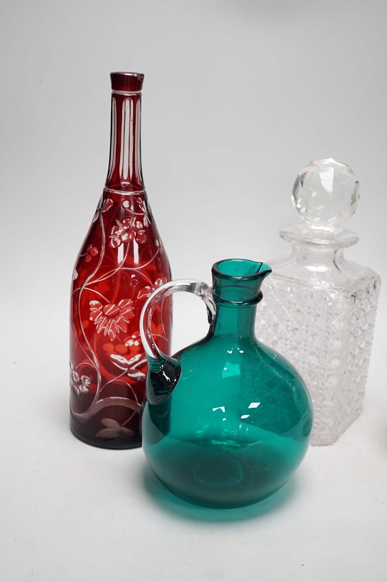A green glass decanter flagon, a Bohemian red flash cut carafe (lacking stopper), a pineapple cut glass decanter and a square hobnail cut glass decanter (4). Tallest 30cm